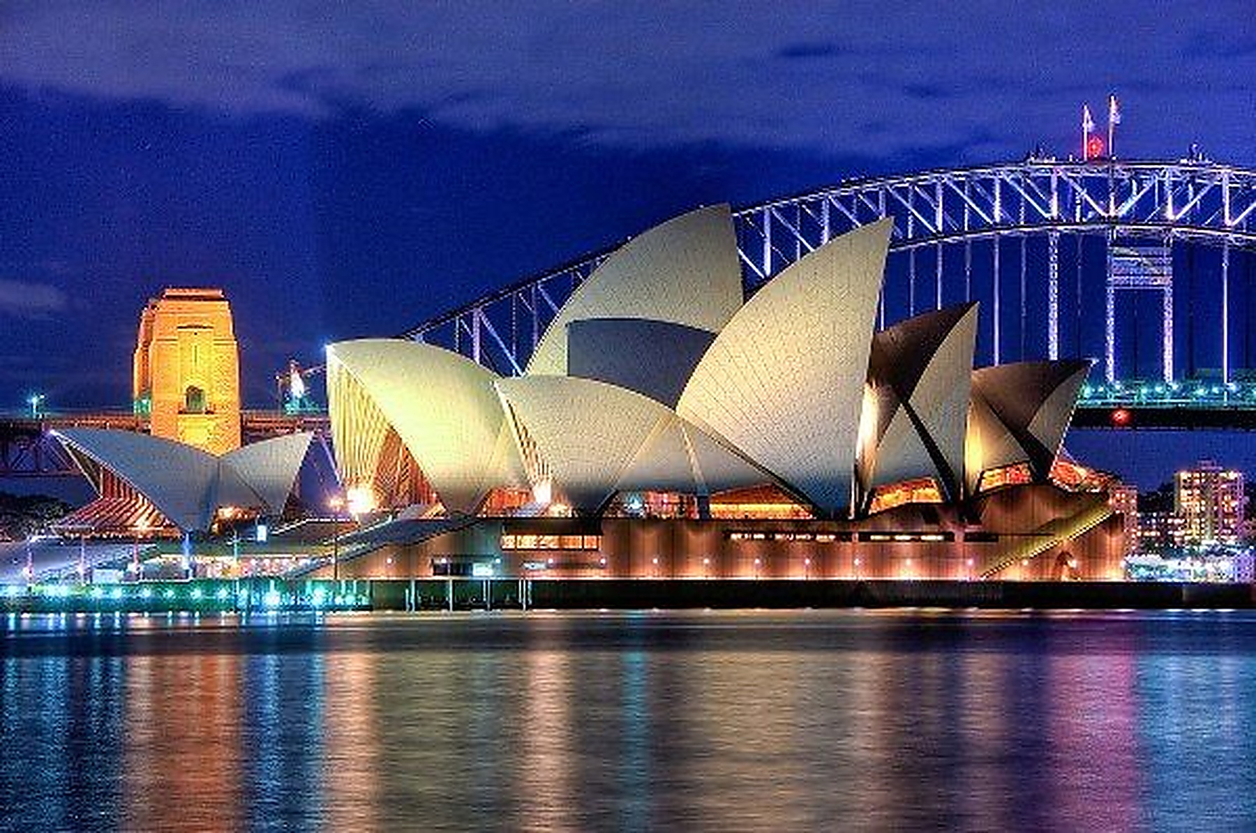 The Sydney Opera House illuminated with golden reflections across the harbour at night